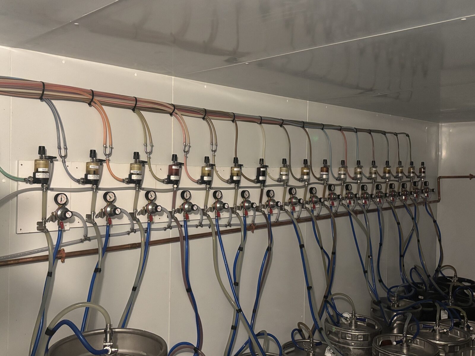 Wall of gas regulators and color-coded distribution lines feeding a multi-keg walk-in cooler